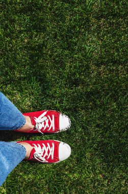 Yeşil çimenlerin üzerinde eski kırmızı spor ayakkabılar bacaklar. Yukarıdan görüntüleyin. Co