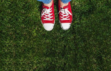 Yeşil çimenlerin üzerinde eski kırmızı spor ayakkabılar bacaklar. Yukarıdan görüntüleyin. Co