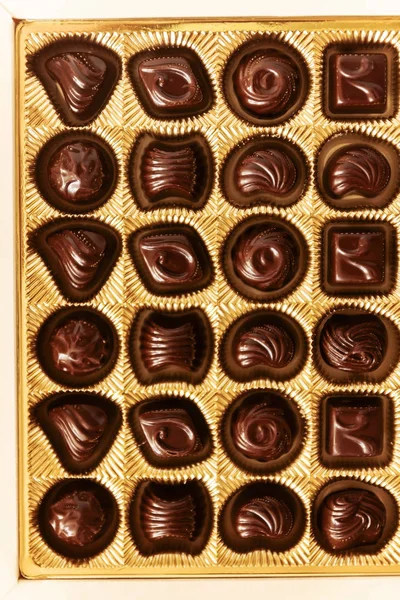 Dulces de chocolate de diferentes formas en una caja de oro, vista superior, s — Foto de Stock
