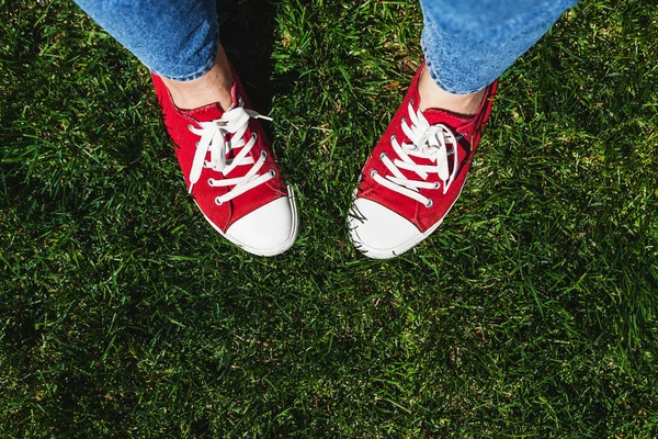 Legs in old red sneakers on green grass. View from above. The co — Stock Photo, Image
