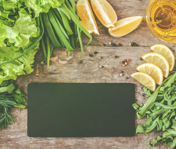 Wooden old background around greens, leaves, lettuce, lemon, oli