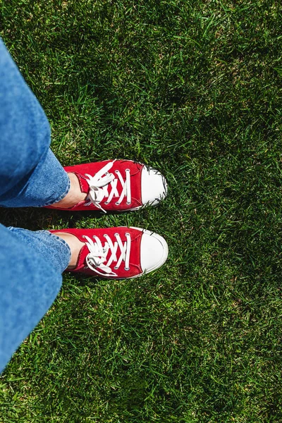 Legs in old red sneakers on green grass. View from above. The co — Stock Photo, Image