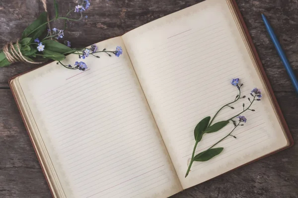 Na staré dřevěné pozadí leží starý notebook a o kytici — Stock fotografie