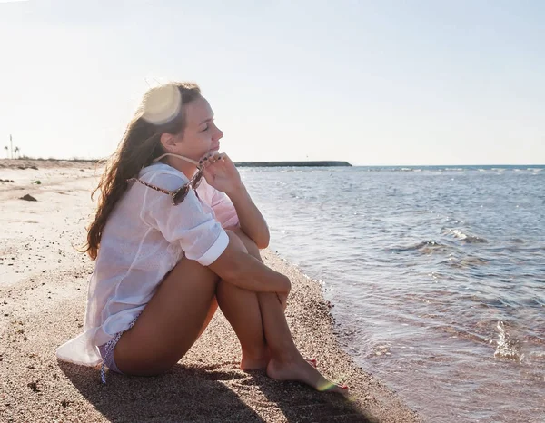 Young woman with a pensive look sits on the seashore. The concep — Stock Photo, Image