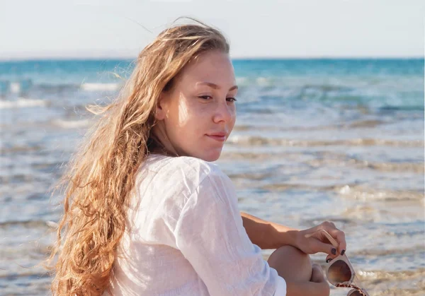 Young woman with a pensive look sits on the seashore. The concep
