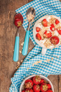 Bir fincan yoğurt, yulaf granola ve bir blu üzerinde taze çilek