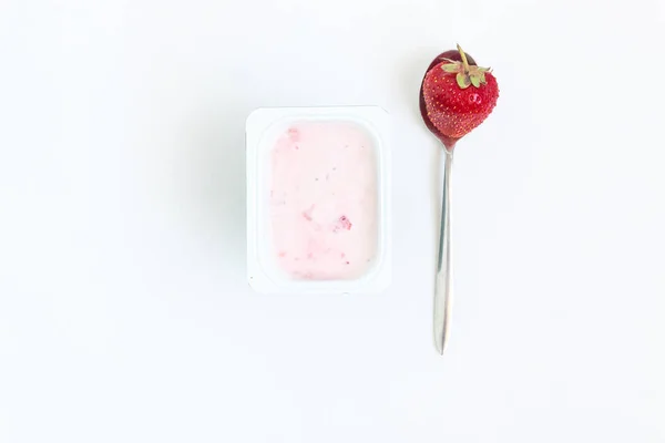 Envase con yogur de fresa y una cuchara con una fresa — Foto de Stock