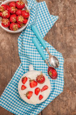 Bir fincan yoğurt ve mavi kaşık havlu üzerinde taze çilek