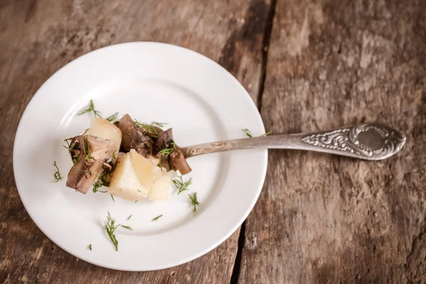 Dish of potatoes with mushrooms on a wooden background — Stock Photo, Image