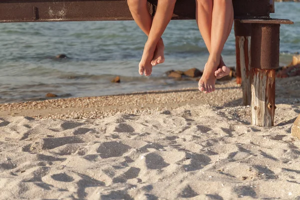 Two pairs of legs dangling over the beach sand — Stock Photo, Image
