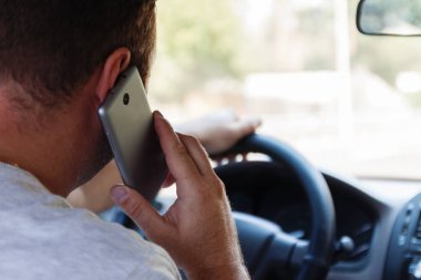 bir araba sürüş sırasında cep telefonuyla konuşan adam