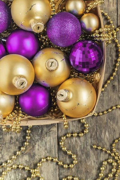 Bolas de Natal roxo e ouro, contas mentira em uma cesta de madeira para — Fotografia de Stock