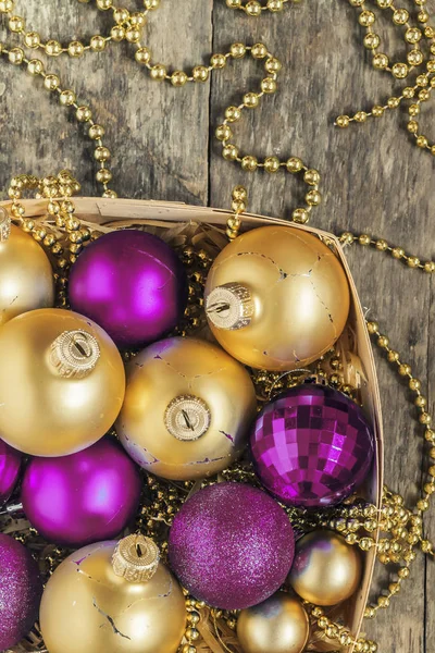 purple Christmas balls and gold, beads lie in a wooden basket to