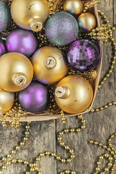 Bolas de Natal roxo e ouro, contas mentira em uma cesta de madeira para — Fotografia de Stock