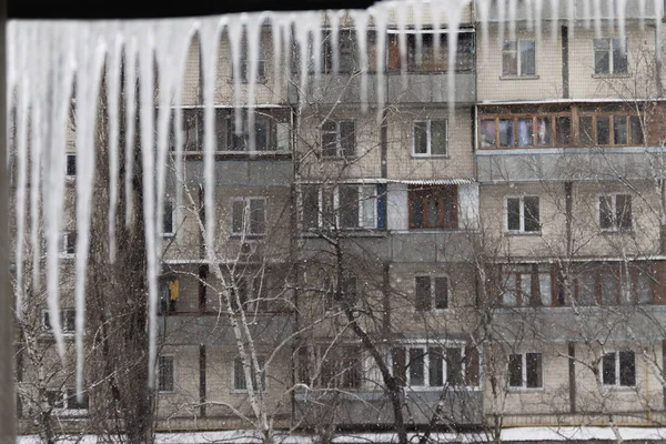 Dangerous icicles hang from the snowy roof of the house. Big ici — Stock Photo, Image