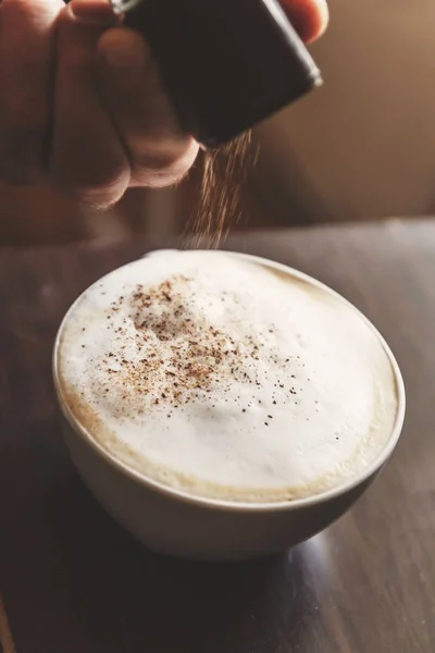 La mano spruzza spezie caffè-cappuccino, cannella, cioccolato — Foto Stock