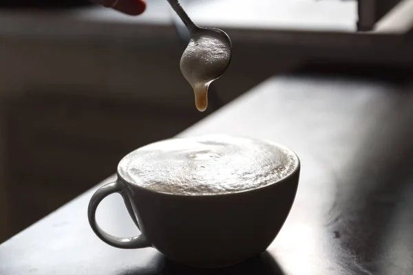Tazza di caffè con schiuma agitata da una mano umana — Foto Stock
