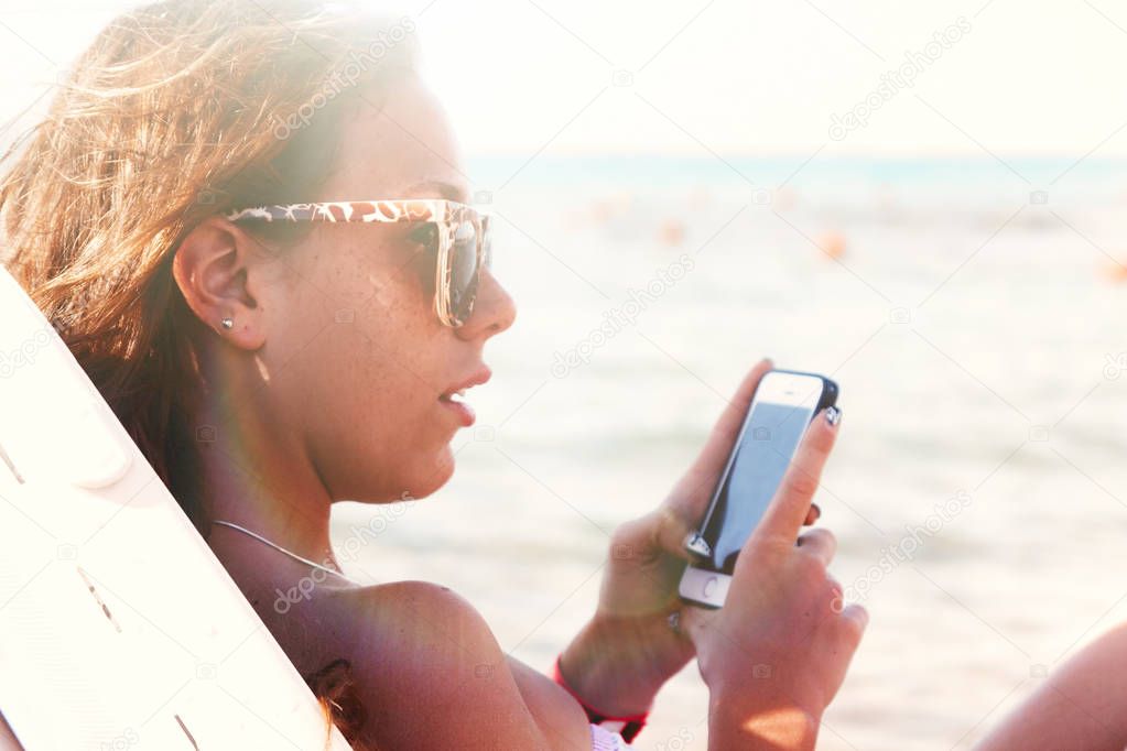 A young tanned woman looks into a smartphone through sunglasses 