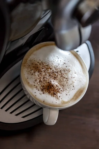 White cup standing on the grating of coffee machine with coffee