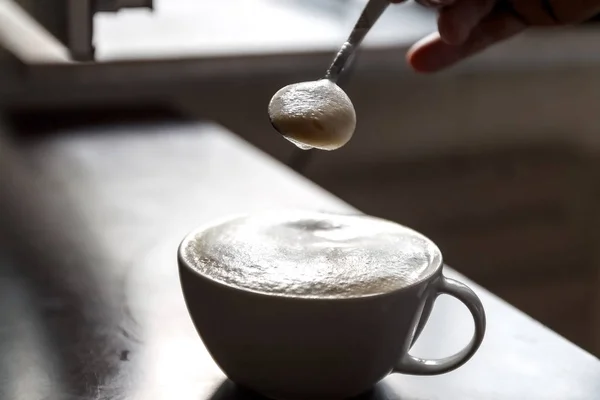 Tazza di caffè con schiuma agitata da una mano umana — Foto Stock