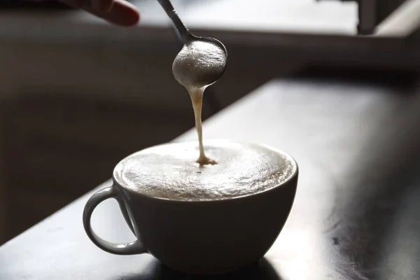 Tazza di caffè con schiuma agitata da una mano umana — Foto Stock