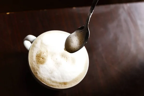 Kopje koffie met schuim wordt geroerd door een menselijke hand — Stockfoto