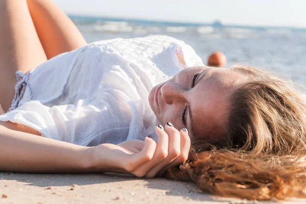 Joven adulto bronceada rubia chica se encuentra en la arena en la playa cerca —  Fotos de Stock