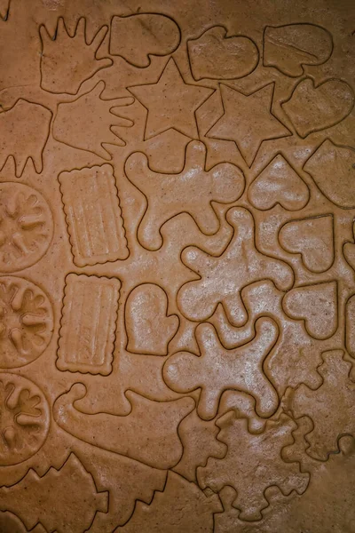 cut out gingerbread cookie in the form of a Christmas tree, star, little man, hearts from raw dough on parchment baking paper on a dark background. Top view. save space