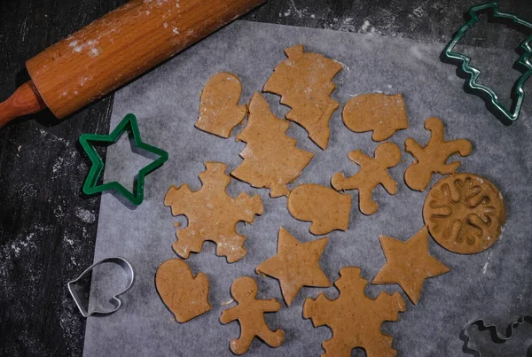 Cut out gingerbread cookie in the form of a Christmas tree, star, little man, hearts from raw dough on parchment baking paper on a dark background. Top view. save space — Stock Photo, Image