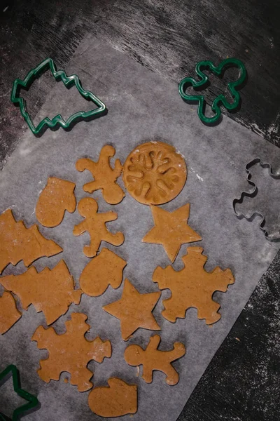Cut out gingerbread cookie in the form of a Christmas tree, star, little man, hearts from raw dough on parchment baking paper on a dark background. Top view. save space — Stock Photo, Image