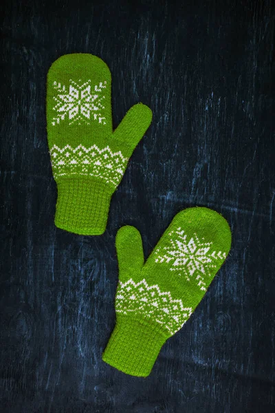 Ein Paar blau-grüne Strickhandschuhe auf einem dunkelblau-grün-braunen Holz — Stockfoto