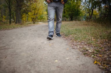 Kot pantolonlu ve spor ayakkabılı erkek bacakları yere doğru yürüyordu. Her tarafı sarı yapraklarla kaplıydı. Sonbahar varış konsepti, yakın plan, kopyalama alanı.