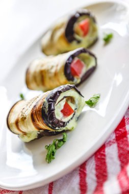 hafif bir arka plan üzerinde beyaz bir tabak üzerinde kızarmış patlıcan, süzme peynir ve domates geleneksel çanak üç rulo. Minimalizm. Yukarıdan görüntüle