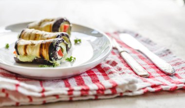 hafif bir arka plan üzerinde beyaz bir tabak üzerinde kızarmış patlıcan, süzme peynir ve domates geleneksel çanak üç rulo. Minimalizm. Yukarıdan görüntüle