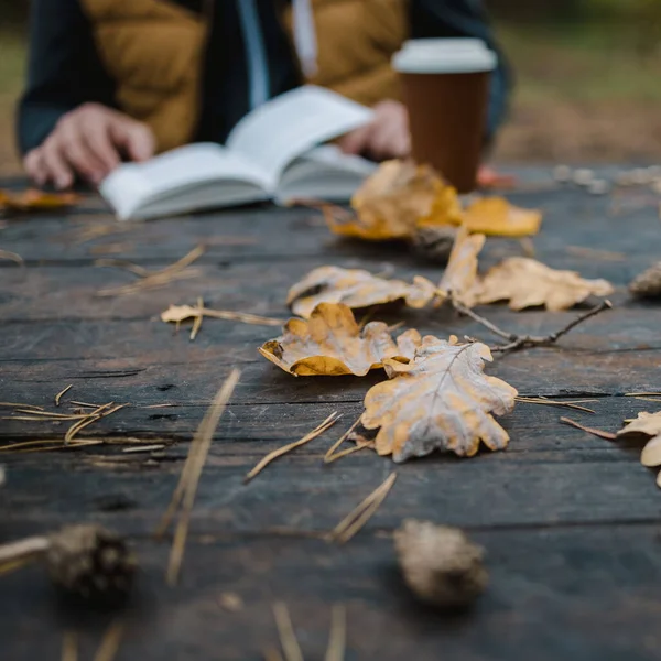 Férfi nő olvas egy könyvet az őszi parkban iszik elvitelre kávét. Közelkép a válla fölött, elmosódott. felülnézet, helyet takarít meg. Láttam a kezeit. Sötét retro stílusban — Stock Fotó