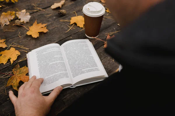 Male female reads a book in autumn park drinks takeaway coffee coffee. Close-up over shoulder, blurred. top view, save space. Seen hands. In a dark retro style — Stock Photo, Image