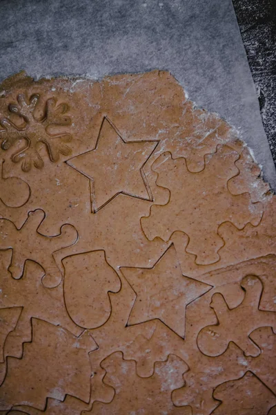 Cut out gingerbread cookie in the form of a Christmas tree, star, little man, hearts from raw dough on parchment baking paper on a dark background. Top view. save space — Stock Photo, Image