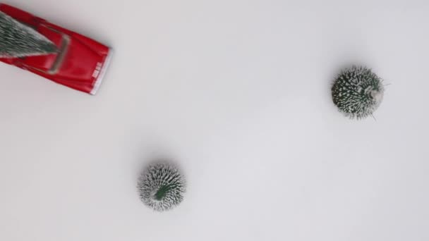 Červené miniaturní autíčko nese vánoční stromek na bílém zasněženém pozadí. Horní pohled. Rozumím. Zpomal. Koncepce, oslava Vánoc a Nového roku.