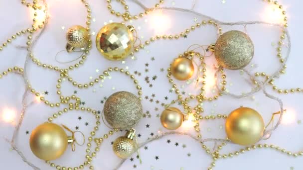 Christmas golden decor on a white background and a garland blinking with lights in blur. View from above. Fixated. Concept, Christmas and New Year celebration. — Stockvideo