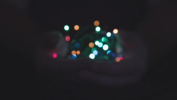 Burning festive christmas garland with lights in male hands on a dark background.Selective focus, blur, retro-toning. Fixated. Concept, Christmas and New Year celebration. — Stock Video