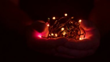 Erkeğin elinde ışıklarla yanan Noel çelengi. Karanlık bir arka plan. Seçici odak, bulanıklık, retro-ton. Takıntılı. Kavram, Noel ve Yeni Yıl Kutlaması.