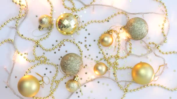 Christmas golden decor on a white background and a garland blinking with lights in blur. View from above. Fixated. Concept, Christmas and New Year celebration. — Stockvideo