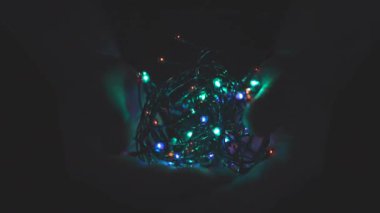 Erkeğin elinde ışıklarla yanan Noel çelengi. Karanlık bir arka plan. Seçici odak, bulanıklık, retro-ton. Takıntılı. Kavram, Noel ve Yeni Yıl Kutlaması.