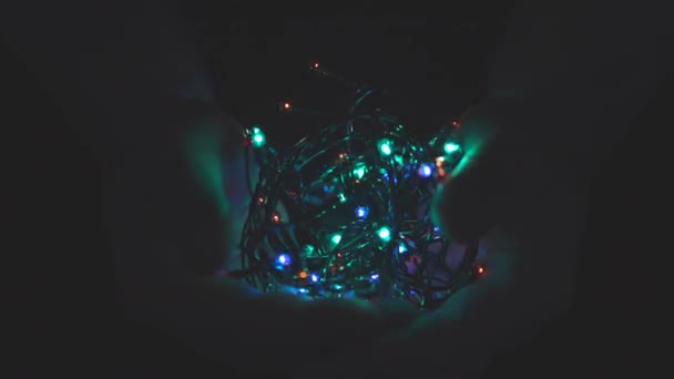 Burning festive christmas garland with lights in male hands on a dark background.Selective focus, blur, retro-toning. Fixated. Concept, Christmas and New Year celebration. — Stock Video