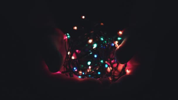 Burning festive christmas garland with lights in male hands on a dark background.Selective focus, blur, retro-toning. Fixated. Concept, Christmas and New Year celebration. — Stock Video