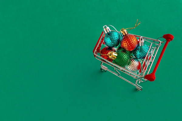 Grocery cart with Christmas balls toys on a blue-green simple background. Flat lay. Save the space. Postcard Template