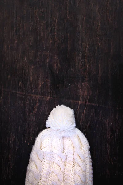 Knitted white hat with balabon on a dark wooden background with copy space. View from above — Stock Photo, Image