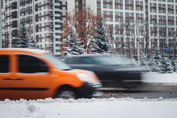 a car in motion rides along a tall building on a winter road in snow