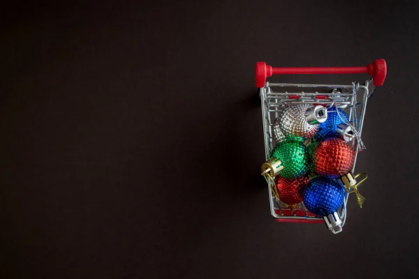 Grocery cart with Christmas balls toys on a dark simple background. Flat lay. Save the space. Postcard Template