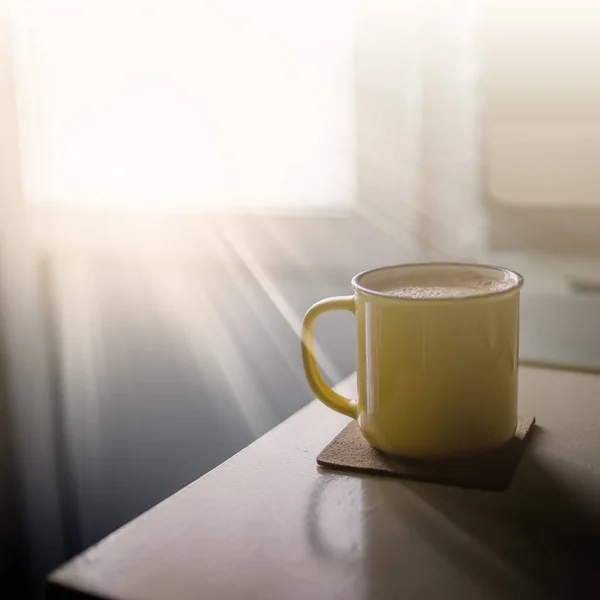 Eine gelbe Tasse Kaffee steht auf dem Schreibtisch im sonnigen Morgen- und Abendlicht neben Monitor und Tastatur — Stockfoto